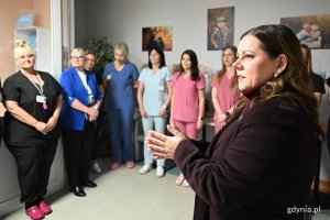 Kobieta w wiśniowym płaszczu w towarzystwie pielęgniarek