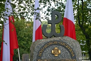 Symbol Polski Walczącej oraz napis "Bóg - honor - ojczyzna" na pomniku Armii Krajowej na skwerze Kościuszki. W tle gałęzie drzew oraz biało-czerwone flagi // fot. Magdalena Czernek