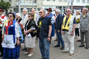 Osoby w ludowych strojach pod pomnikiem