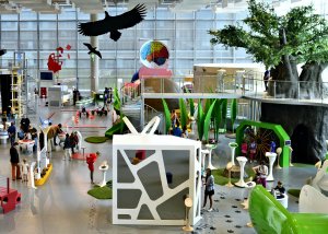 Wnętrze Centrum Nauki Experyment pełne eksponatów i wystaw, pośród nich spacerujący widzowie. 