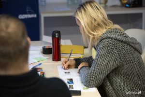 Uczestniczka warsztatów notuje, siedząc przy stole.