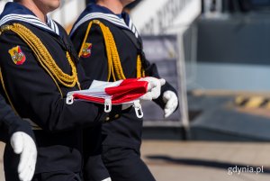 Marynarze niosą złożonż flagę, kt&oacute;ra następnie wciągną na maszt
