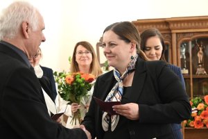 Kobieta z apaszką na szyi gratuluje starszemu panu