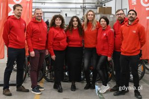 Grupa osób stojących w rzędzie na tle rzędu rowerów