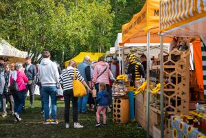 Ludzie spacerują w parku, oglądając stragany z produktami żywnościowymi, jak miody.