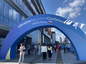 Baner Konferencji Odbudowy Ukrainy (Ukraine Recovery Conference) w Gdańsku  i przechodzący pod nim ludzie