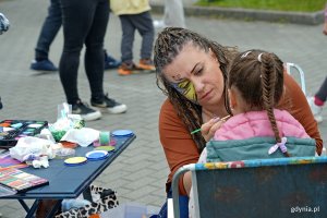 Kobieta malująca wzór na twarzy dziewczynki podczas festynu „Jestem kibicem” 