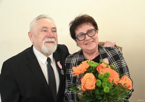 Starszy pan w garniturze, obejmuje kobietę w okularach z bukietem kwiat&oacute;w