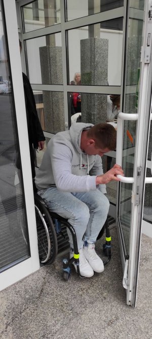 Policjant na wózku inwalidzkim próbuje wyjechać z budynku urzędu