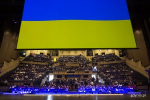 Ekran, na którym jest wyświetlona ukraińska flaga, nad sceną Teatru Muzycznego w Gdyni. W tle widownia zgromadzona podczas koncertu // fot. Przemysław Kozłowski