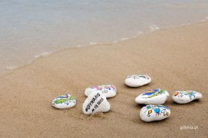 Kamyki malowane w kaszubskie wzory leżą na piasku na plaży
