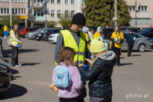 Dwie dziewczynki wrzucają pieniądze do skarbonki, kt&oacute;rą trzyma młody chłopiec w ż&oacute;łtej koszulce