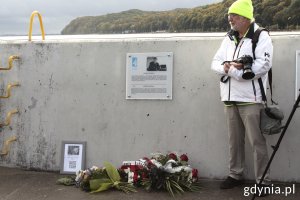 Tablica kapitana Andrzeja Drapelli w gdyńskiej alei Żeglarstwa Polskiego, pod nią kwiaty, a obok stoi fotograf 
