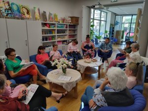 Uczestnicy Narodowego Czytania w Bibliotece Chylonia siedzą w fotelach ustawionych dookoła dwóch stolików // fot. materiały prasowe