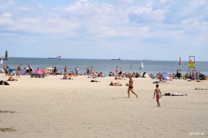 Plaża, ludzie i morze. W oddali stojące statki cargo. 