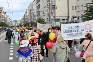 Uczestnicy przemarszu w ramach V Pomorskiego Dnia Seniora idący ul. Świętojańską. W kolorowych strojach i z balonami w rękach.