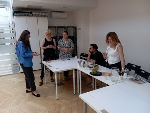 Cztery kobiety i jeden mężczyzna, rozmawiają i patrzą na zdjęcia, które leżą na stole.