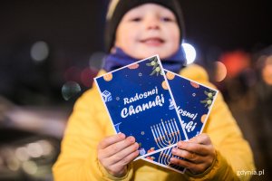 Dziecko trzyma kartki okolicznościowe z napisem "Radosnej Chanuki"