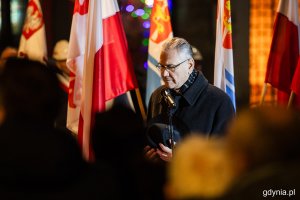 Mężczyzna stojący przy mikrofonie przed pomnikiem