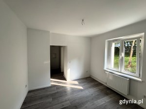 Na zdjęciu widać salon mieszkania, w dalszym planie widoczne są również okna.
