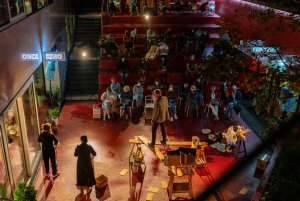 Troje aktorów stoi na czerwonym patio Gdyńskiego Centrum Filmowego. Obok nich są teatralne rekwizyty. W tle czerwone schody i siedząca publiczność // fot. Anna Rezulak
