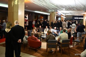 Kilkadziesiąt os&oacute;b, stojących i siedzących we foyer Hotelu Mercure Gdynia 