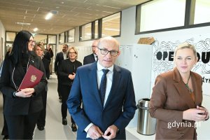 Grupa elegancko ubranych osób idąca po przestronnym korytarzu