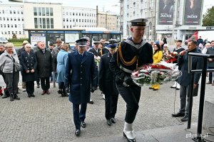Przedstawiciele służb mundurowych podczas składania kwiatów pod tablicą pamiątkową na fasadzie Dworca PKP Gdynia Główna 