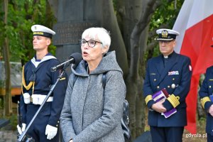  Joanna Zielińska - przewodnicząca Rady Miasta Gdyni przemawia podczas obchodów 80. rocznicy zbrodni katyńskiej. W tle powiewa biało-czerwona flaga i stoją: żołnierz oraz kapelan Marynarki Wojennej // fot. Magdalena Czernek