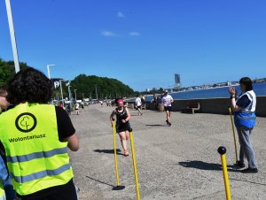 Bulwar w Gdyni, w tle Śródmieście, Sea Towers, tyłem wolontariusz, do mety dobiega zawodniczka