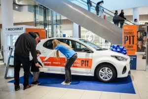 Mężczyzna z małych chłopcem obok auta, dziewczyna w niebieskiej koszuulce podaje mu ulotkę