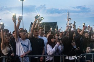 Grupa młodych ludzi trzymających w rękach telefony z zapalonymi latarkami podczas koncertu