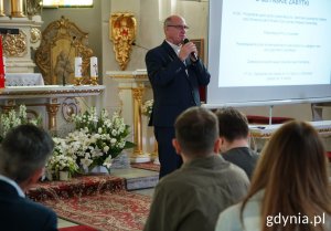 Ks. kan. Kazimierz Glama z mikrofonem na tle ołtarza
