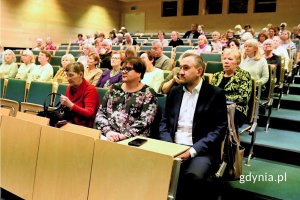 Wiele osób siedzących w rzędach krzeseł w auli