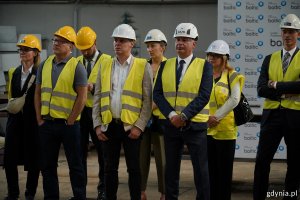 Grupa osób w kaskach i kamizelkach na symbolicznej uroczystości cięcia stali 