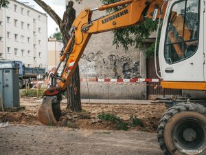 na pierwszym planie koparka wykonuje roboty drogowe, w tle prace drogowe