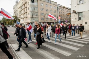 Uczestnicy akcji "Stop przemocy przeciwko narodowi Białorusi" idą ulicą Świętojańską w Gdyni. Niektórzy z nich w rękach niosą białoruskie flagi // fot. Karol Stańczak