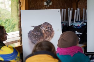 Obraz z wr&oacute;blem i patrzące na niego osoby