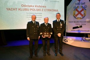 Grupa osób stojących na scenie i mających za plecami biały ekran