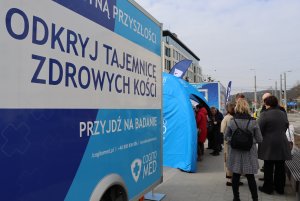 bus z napisem "Odkryj tajemnicę zdrowych kości" w tle rejestrujący się mieszkańcy