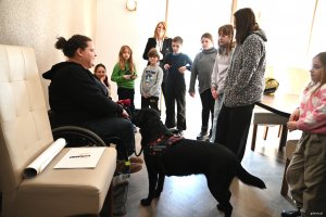 Kobieta na w&oacute;zku inwalidzkim z psem asystującym oraz dzieci