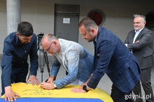 Wiceprezydenci Gdyni: Michał Guć i Marek Łucyk podpisują ukraińską flagę, która pojedzie do Chersonia