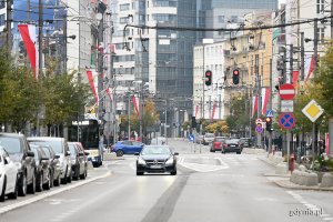 Biało-czerwone flagi na masztach i słupach ozdobią ulicę Świętojańską z okazji Święta Niepodległości. Flagi wiszą po bokach, w centrum zdjęcia ulica Świętojańska i jadące po niej samochody // fot. Michał Puszczewicz