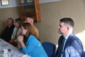 Mężczyźni i kobiety siedzący przy stole z białym obrusem i słuchający prelekcji
