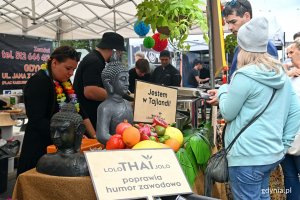 Jedno ze stoisk na festiwalu „Kulinarna Świętojańska”. Na pierwszym planie kolejka klientów oraz owoce i tajskie figurki. Za stołami obsługa serwuje dania // fot. Magdalena Czernek