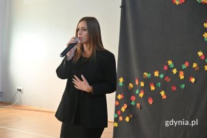 Stojąca kobieta śpiewająca do mikrofonu w szkolnej hali sportowej