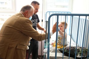W pokoju szpitalnym stoi prezydent Gdyni i tata dziecka, na łóżku siedzi chłopiec i przykłada dłoń do dłoni prezydenta.