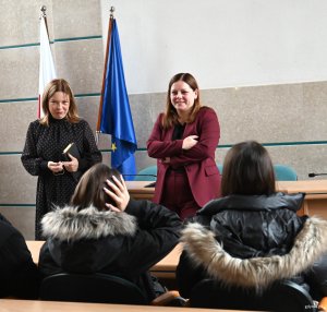 Kobieta w czarnej sukience, obok kobiety w bordowym kostiumie