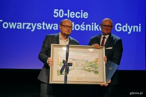 Mariusz Bzdęga &ndash; dyrektor zarządzający ds. kultury i aktywności mieszkańc&oacute;w przekazuje akwarelę Wojciechowi Kodłubańskiemu &ndash; prezesowi Towarzystwa Miłośnik&oacute;w Gdyni podczas uroczystości z okazji 50-lecia towarzystwa 