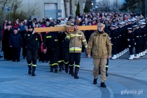Strażacy niosący krzyż i inni uczestnicy Gdyńskiej Drogi Krzyżowej idący za nimi w procesji 
